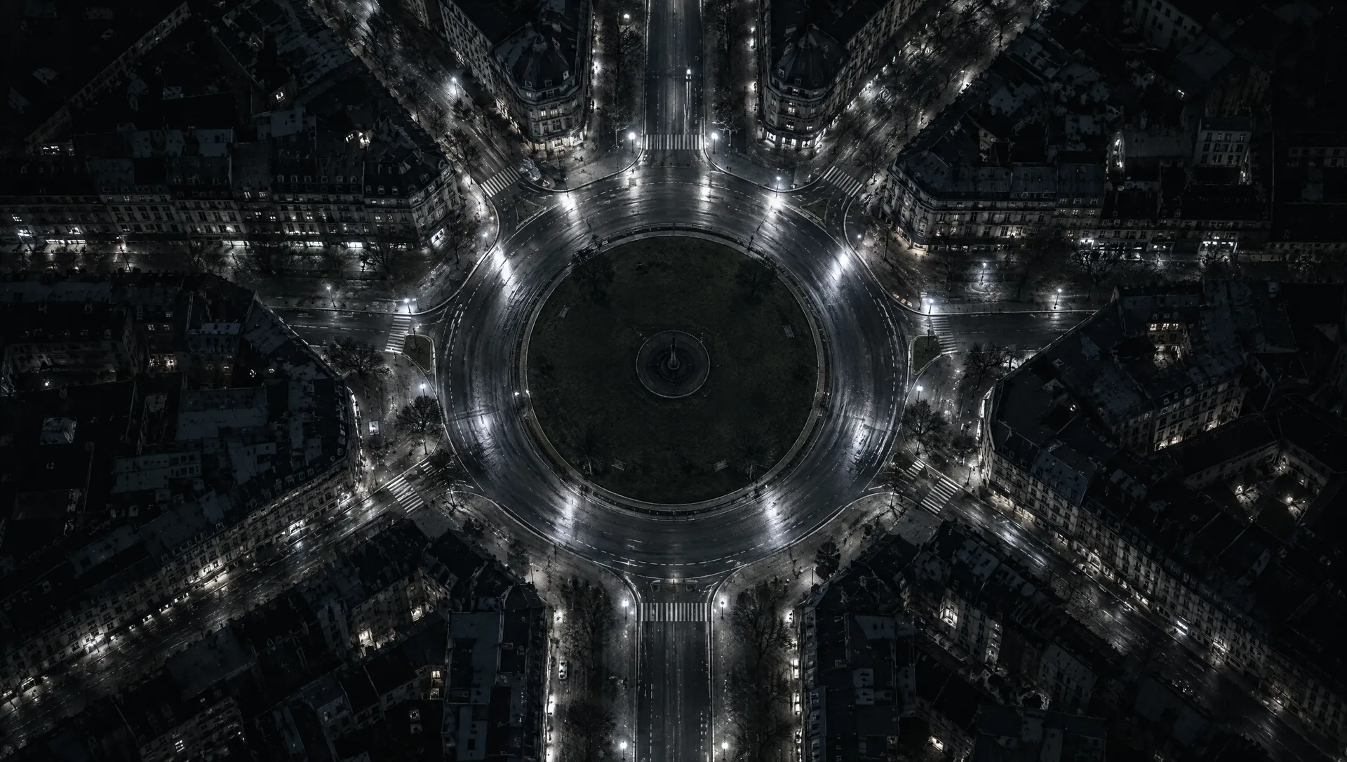 A city roundabout from above at night, streets radiating out.